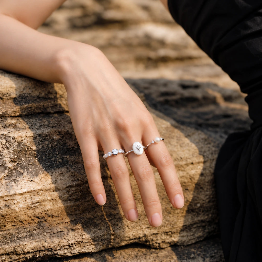 Meteorite Galaxy silver-tone pearl and cubic zirconia rings modeled on a hand against a natural stone background.